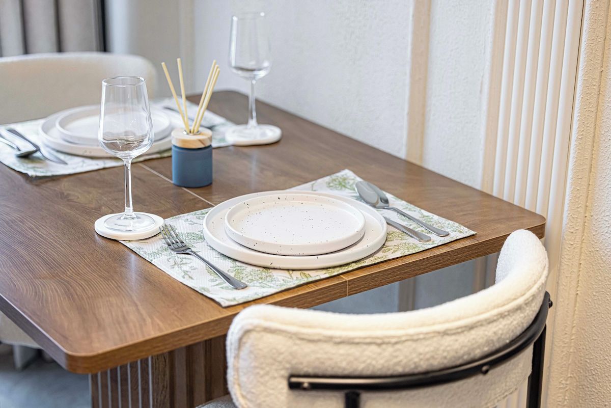 A dining table set with plates, cutlery, and glasses, with a chair positioned at the table.