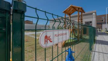 Zona de jocs tancada per una tanca metàl·lica verda amb un cartell que la identifica.