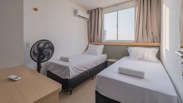 Habitación de hotel con dos camas individuales, una mesita de noche, un ventilador, una ventana con cortinas e instalación de aire acondicionado.