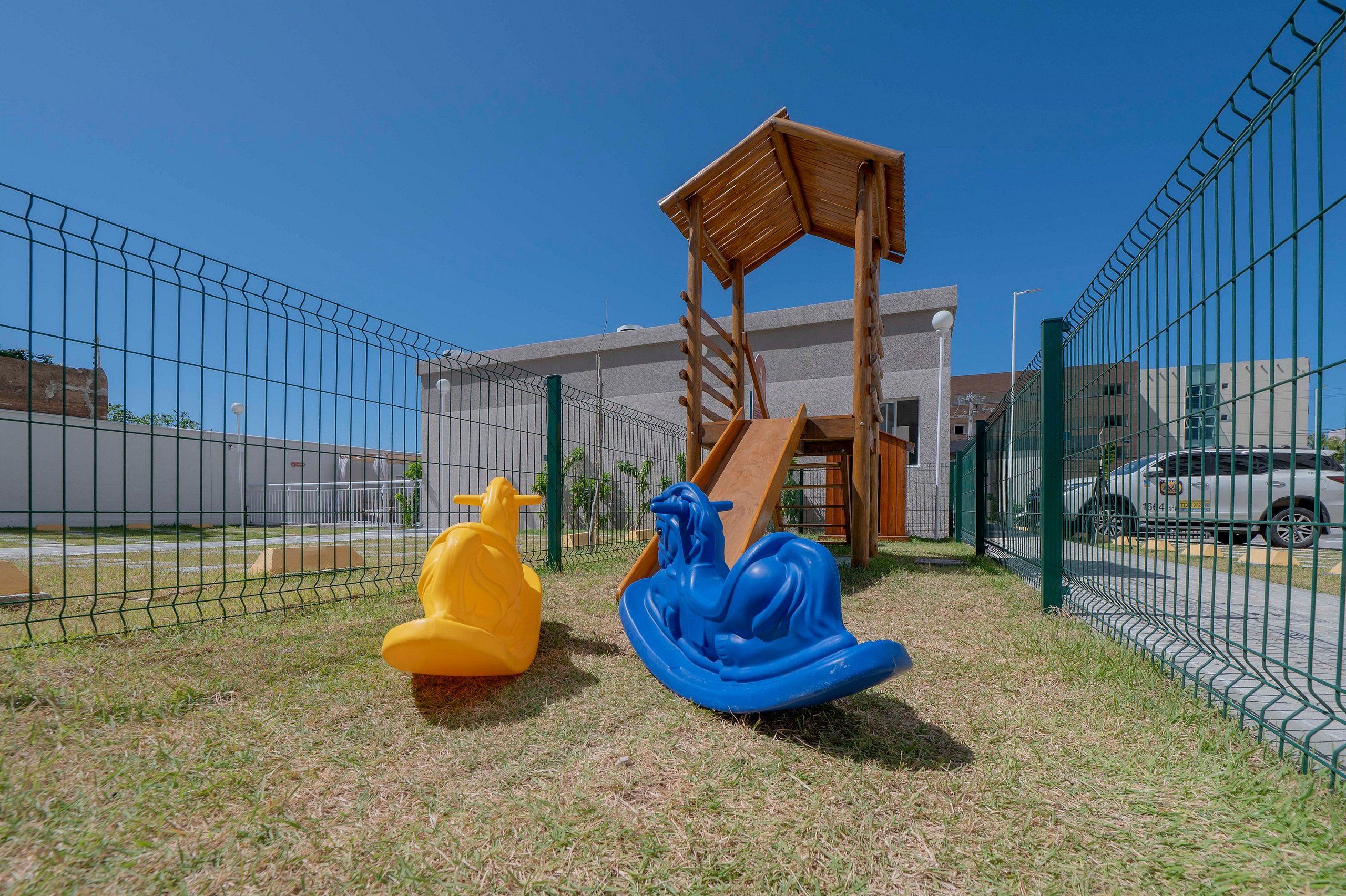A playground with a slide and two swings, enclosed by a fence.