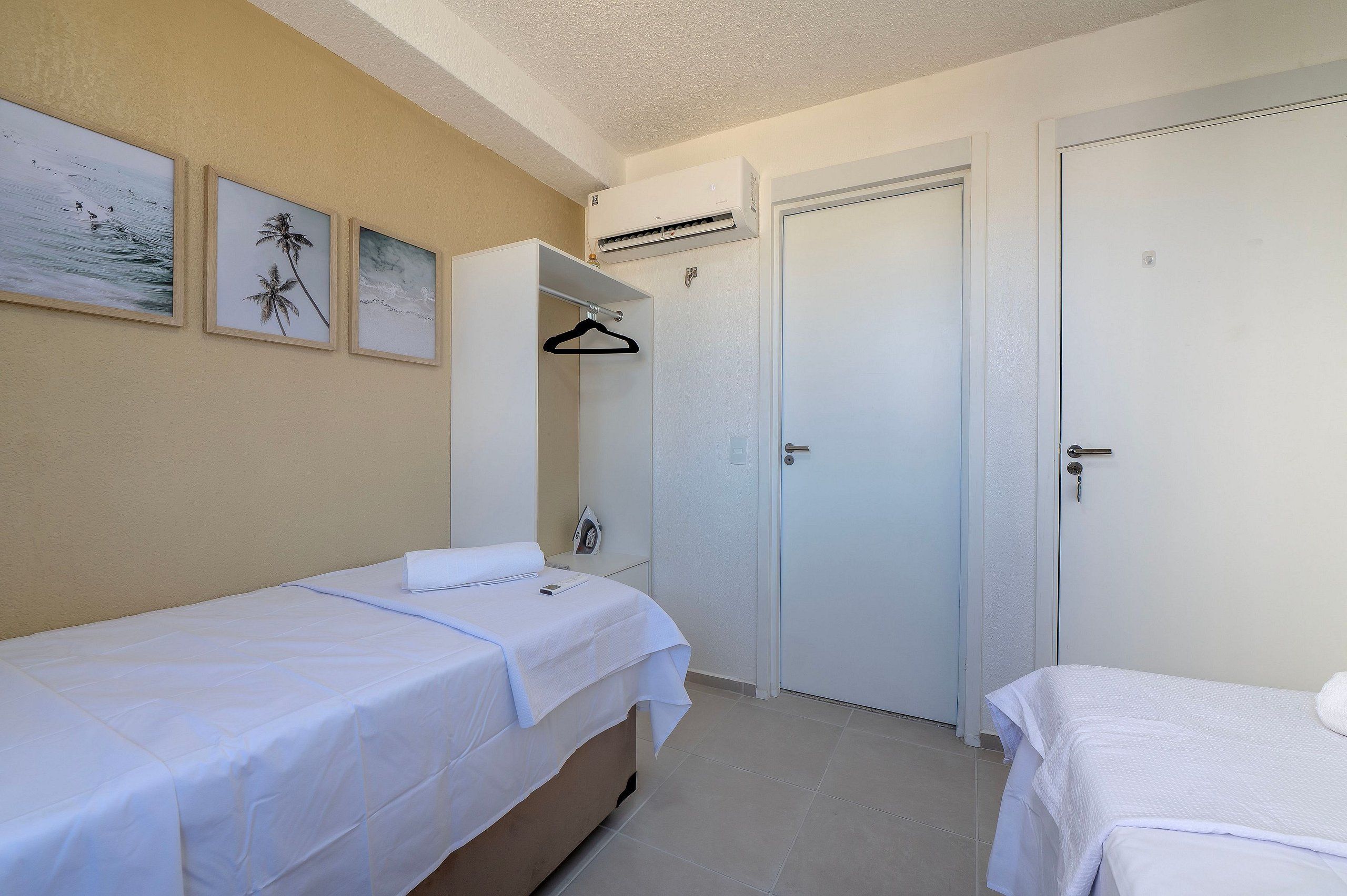 A hotel room with two single beds, a wardrobe, a hanging coat rack, and a wall-mounted air conditioner.