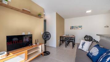Una sala de estar con televisor, ventilador, comedor y sofá con almohadones decorativos.