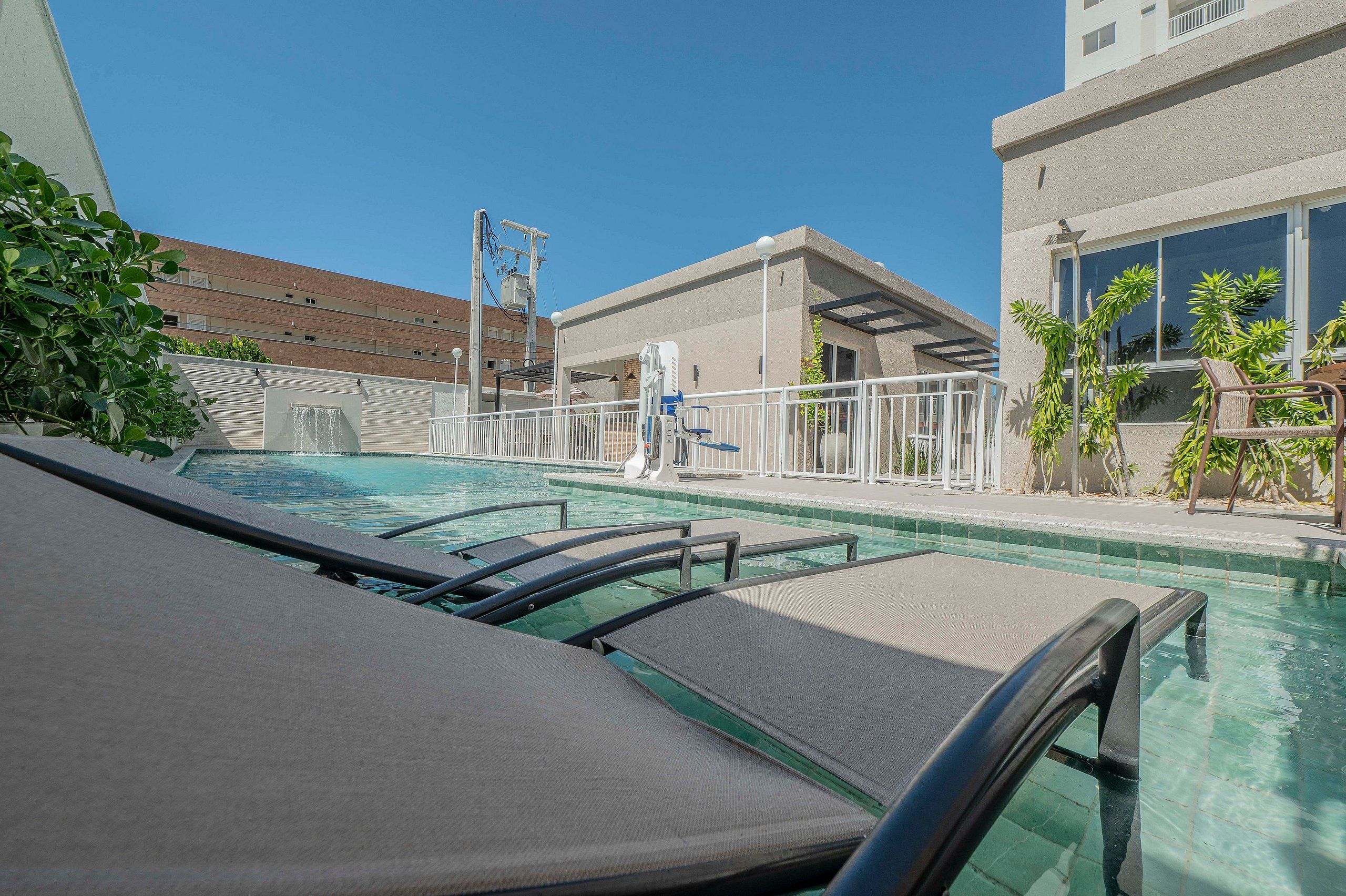 Zona de piscina amb gandules, una font d'aigua i un edifici amb façana de maó al fons.