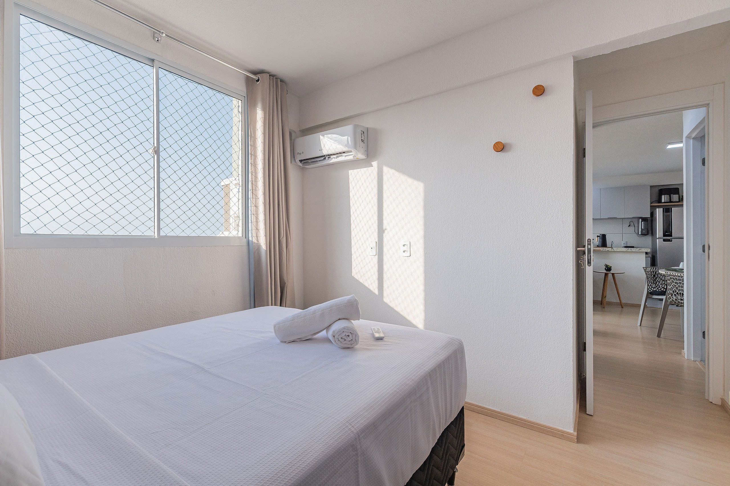 Habitación de hotel con cama, aire acondicionado y vistas a través de una ventana con mosquitera.