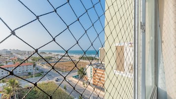Una cerca de malla con vista a una ciudad costera, edificios y un cielo despejado.