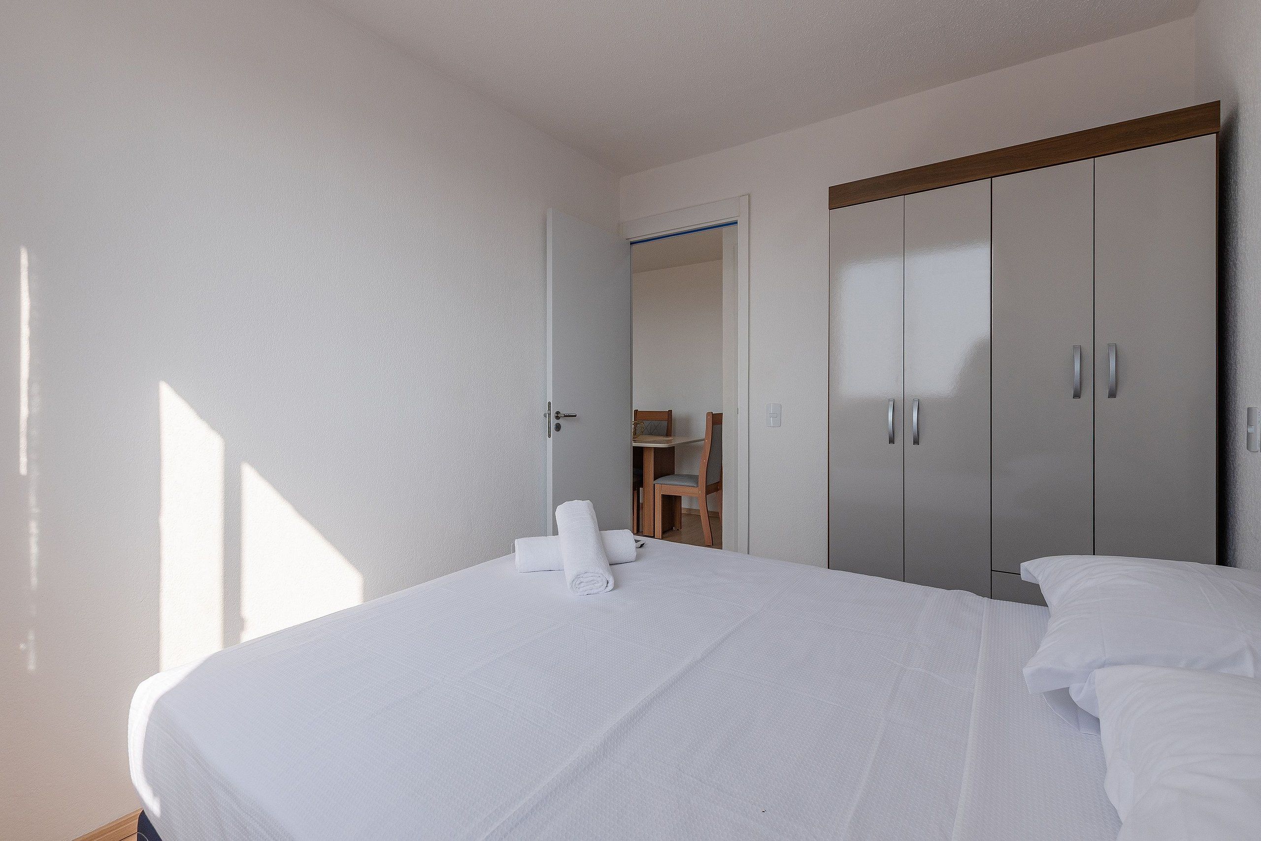 Quarto de hotel com cama, guarda-roupa e uma pequena mesa com toalhas.