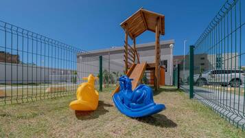 Un parc infantil amb tobogan i dos cadirs d'oscail·lació, tancat per una tanca.