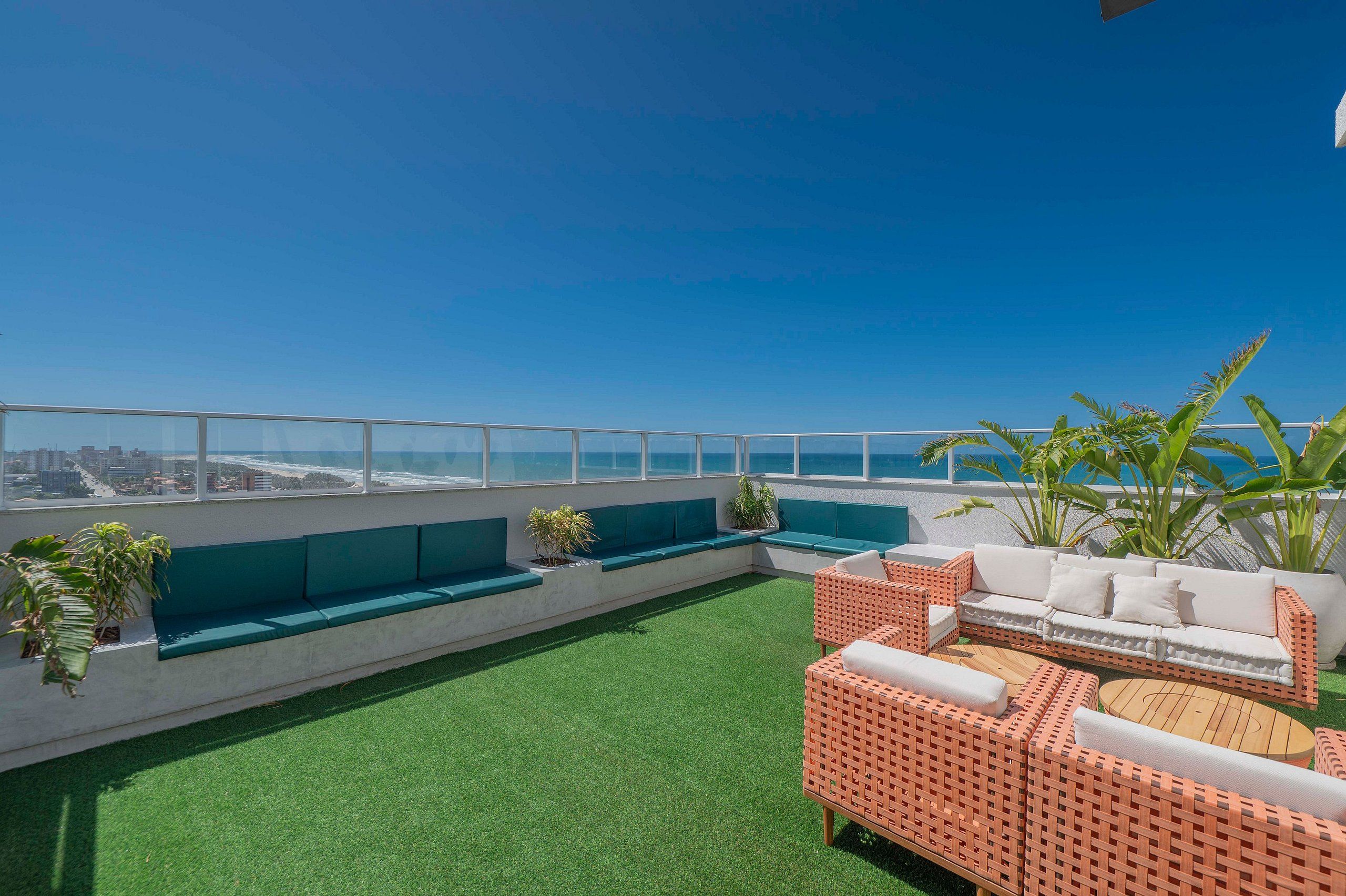 Terraço no telhado com áreas de estar, vista da cidade e plantas tropicais.