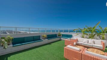 Terraço no telhado com áreas de estar, vista da cidade e plantas tropicais.