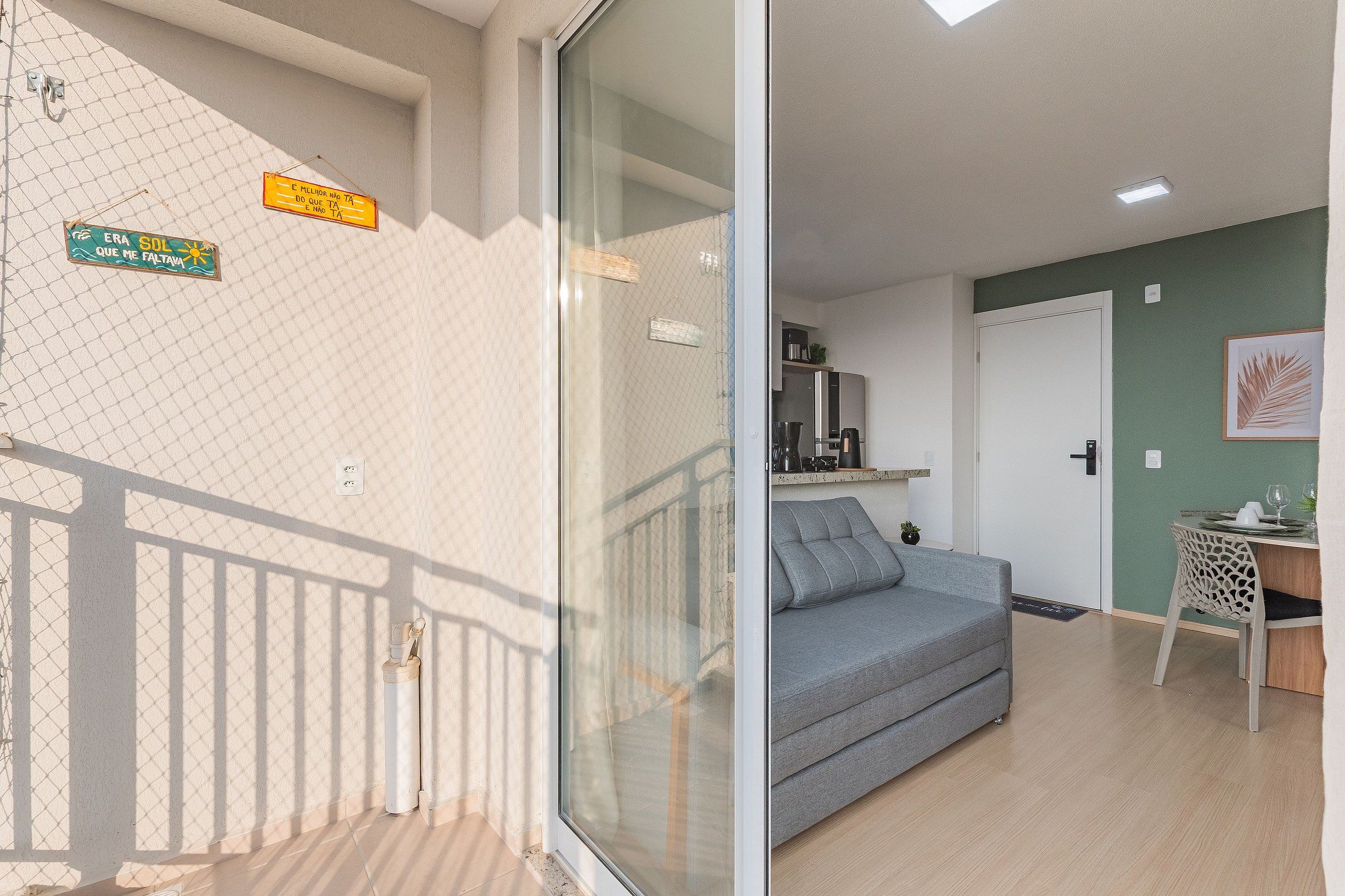 A room with a grey sofa, a small table with a plant, and a kitchen area with appliances.