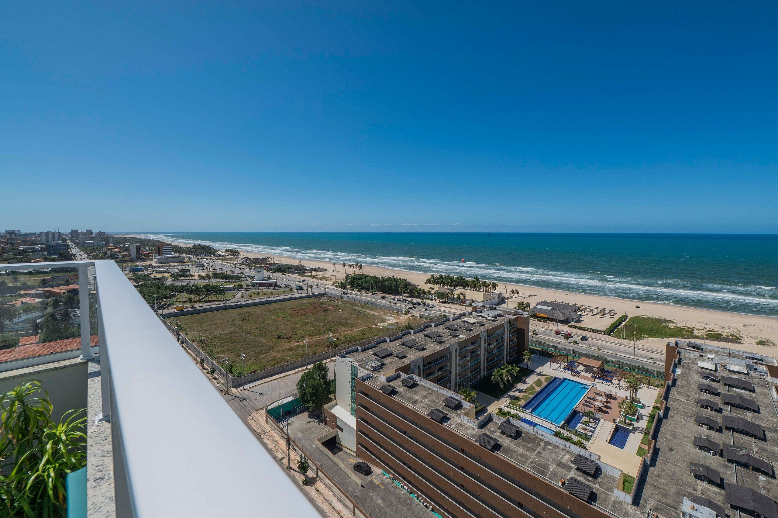 A high-rise hotel with a rooftop pool, a beach view, and a parking area.