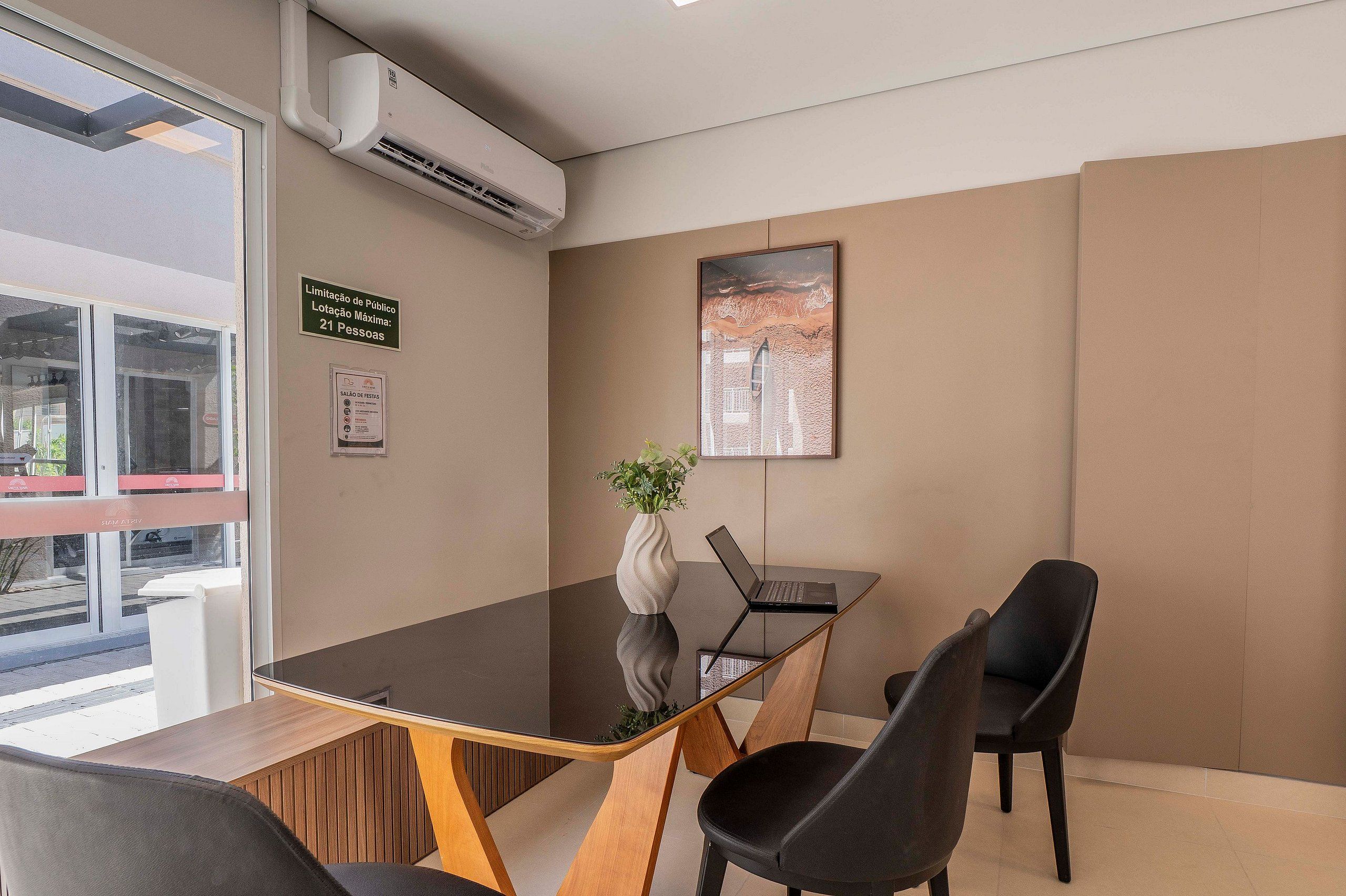 Un salón de conferencias con una mesa de vidrio, sillas negras, una computadora portátil, una planta en maceta y un cuadro en la pared.