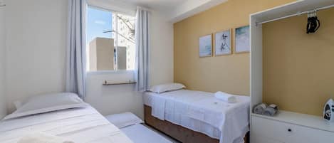 Une chambre d’hôtel avec deux lits, une fenêtre avec des rideaux, un mur orné de tableaux encadrés et une commode blanche avec un fer à repasser.