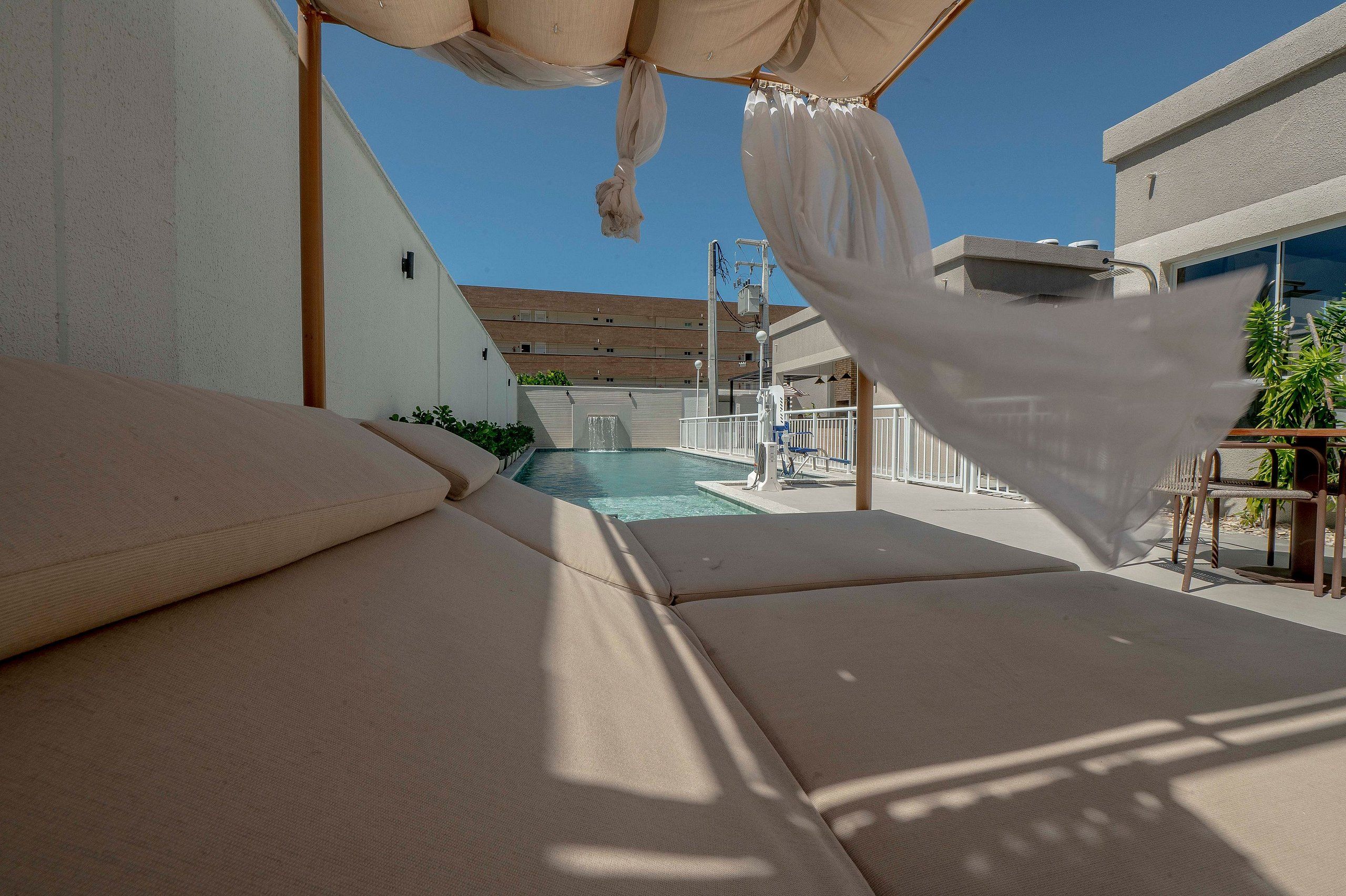 Zona junto a la piscina con una silla de descanso, un toldo y vistas a un edificio con un cartel de números.