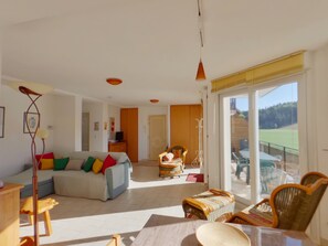 A spacious living room with a sofa, chairs, and a dining table. There is a sliding glass door leading to a balcony. - Peaceful apartment in nature - 4 guests (Morbier)