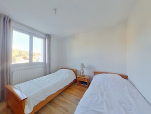 A room with two single beds, a window with curtains, a bedside table with a lamp, and a radiator. - Peaceful apartment in nature - 4 guests (Morbier)