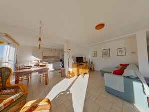 A spacious living area with a sofa, dining table, and chairs. A kitchen is visible in the background. - Peaceful apartment in nature - 4 guests (Morbier)