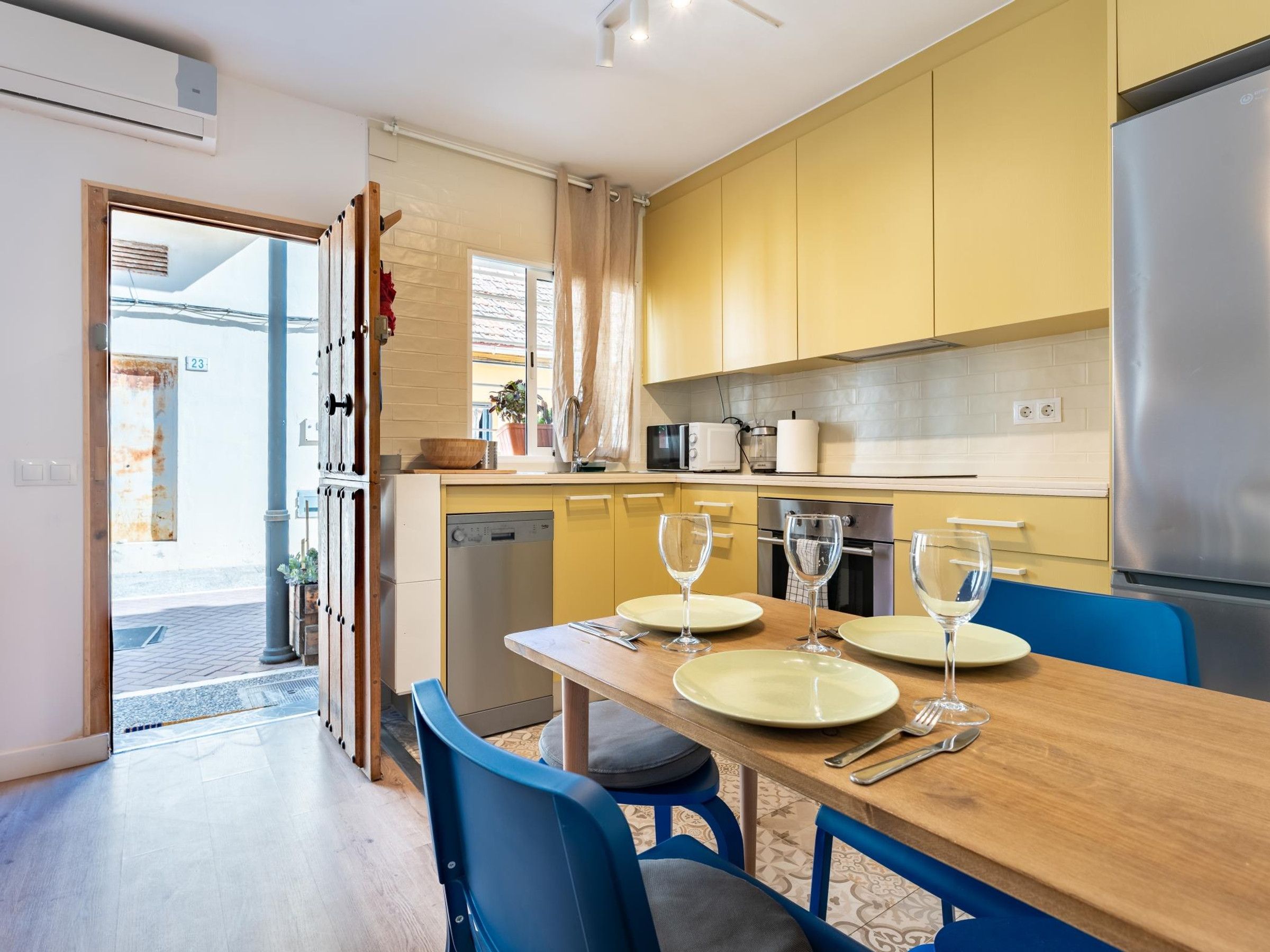 A compact kitchen with yellow cabinets, a stainless steel refrigerator, and a dining table set for two.