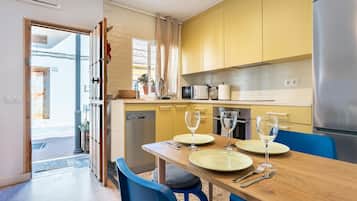 A compact kitchen with yellow cabinets, a stainless steel refrigerator, and a dining table set for two.