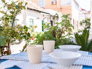 A table with white ceramic cups and bowls, surrounded by potted plants and a blue and white checkered tablecloth. - Traditional house in Pedregalejo - 4 guests (Málaga)
