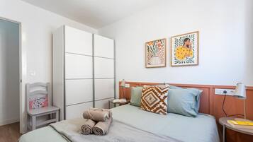 A bedroom with a bed, a nightstand, a chair, a wardrobe, and two wall art pieces.