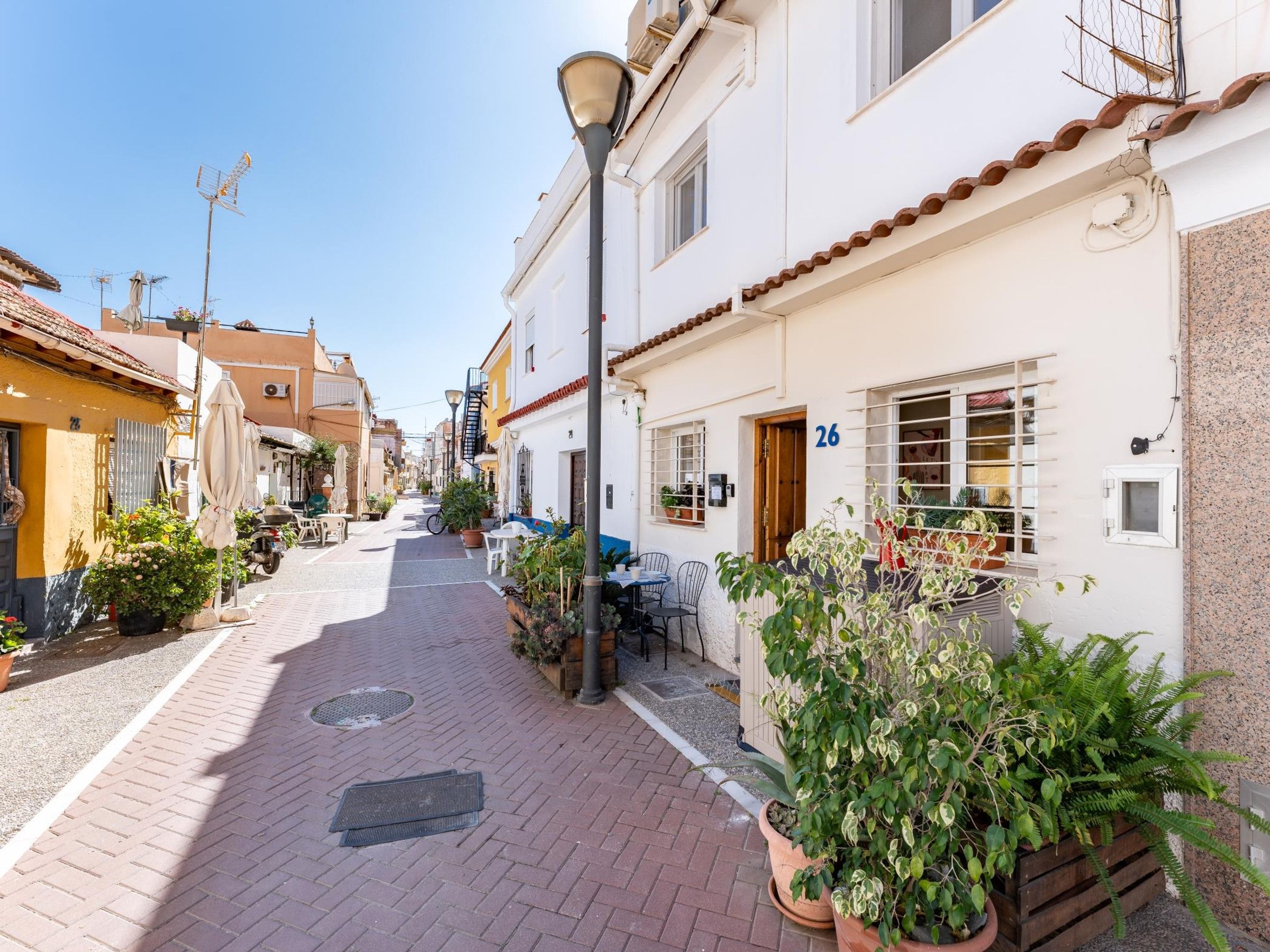 A narrow street lined with buildings, some with balconies and potted plants.