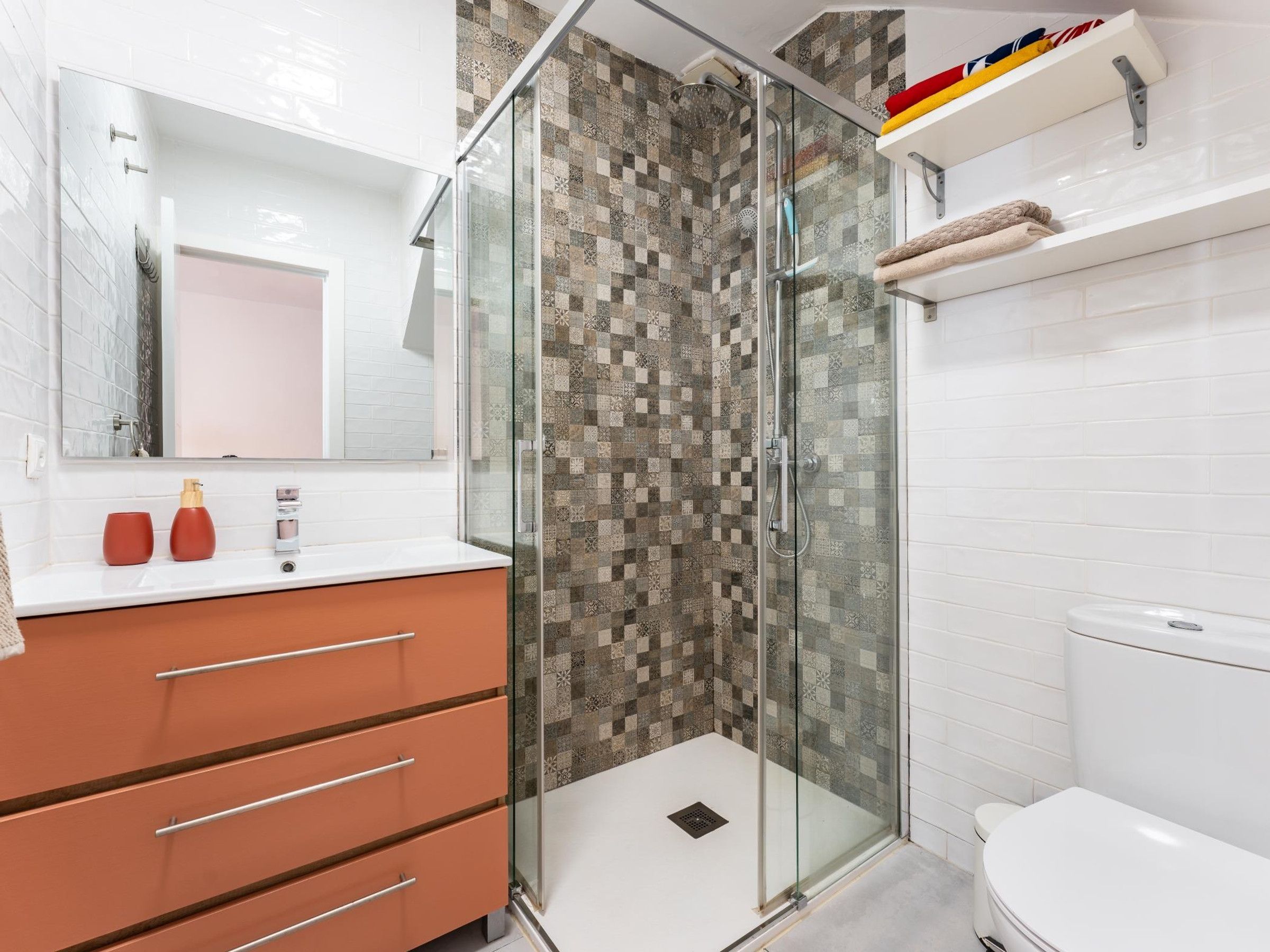 Ein modernes Badezimmer mit einer gläsernen Duschkabine, einer weißen Toilette und einem Waschtisch mit Schubladen.