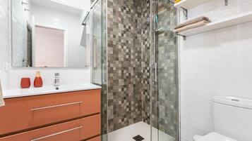 Ein modernes Badezimmer mit einer gläsernen Duschkabine, einer weißen Toilette und einem Waschtisch mit Schubladen.