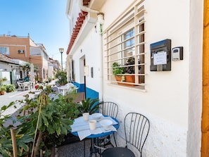 An outdoor seating area with a table and chairs, potted plants, and a window with a view of the street. - Traditional house in Pedregalejo - 4 guests (Málaga)