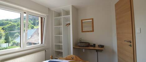 Une chambre à coucher comprenant un lit, une fenêtre, une armoire intégrée, une table de chevet et un miroir.