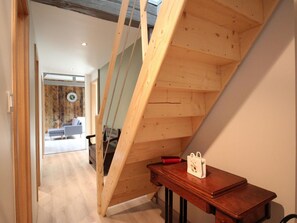 A wooden staircase with a handrail, a wooden table with a bag, and a view into a room with a sofa and a clock. - Spacious house with parking - 14 guests (Rimbach-prés-Masevaux)