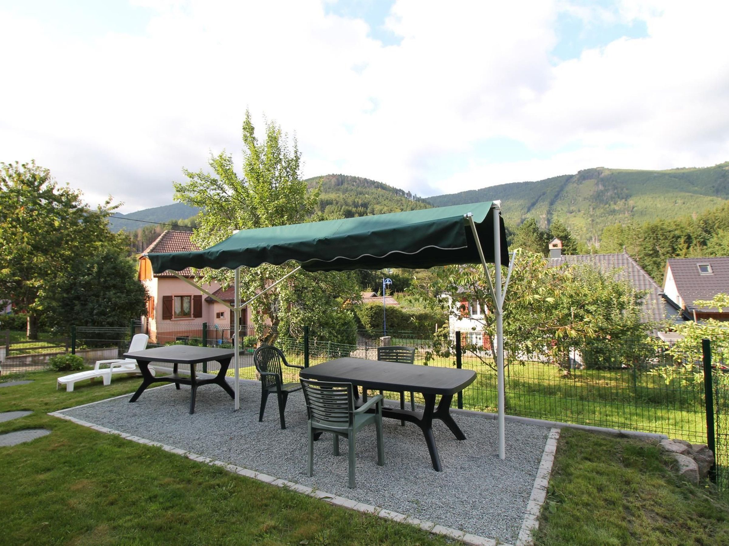 Et udendørs siddeområde med bord og stole, et overdækket picnicbord og udsigt til et bjerrelandskab.