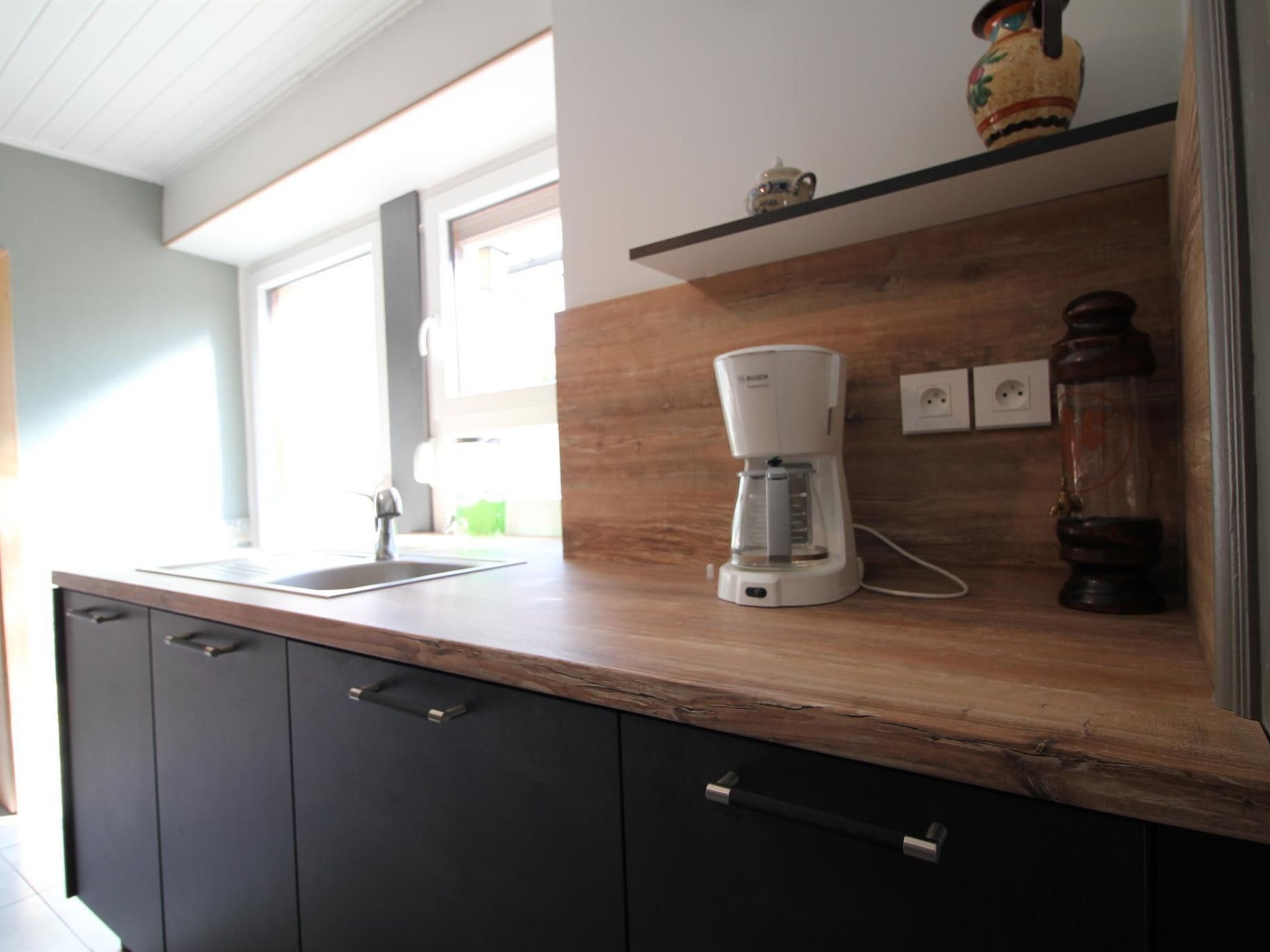 Eine Küche mit Holztischplatte, einer Kaffeemaschine, einem Spülbecken und einem Schrank.