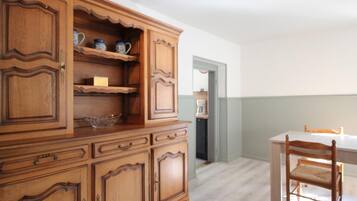 Ein Holzschrank mit vielen Schubladen und Regalen, ein Esstisch mit Stühlen und im Hintergrund ein Küchenbereich.