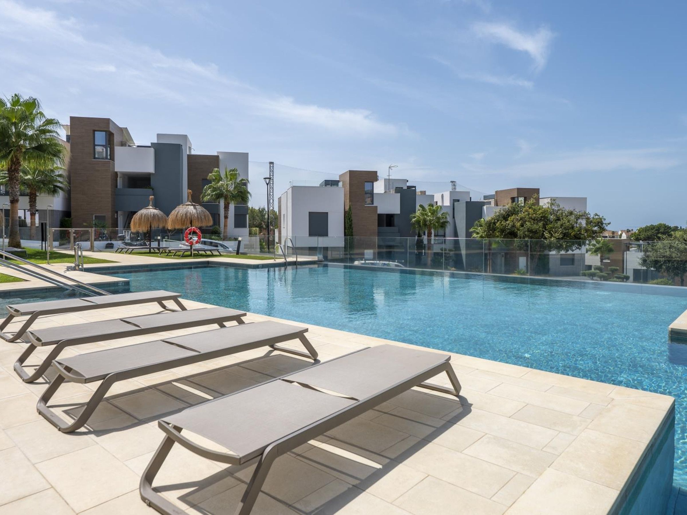 Zona de piscina moderna con sillones de descanso y un cielo azul despejado.