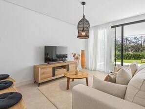A modern living room with a flat-screen TV, wooden furniture, a round coffee table, and a large window with a view of greenery. - Contemporary residence, pets welcome - 6 guests (Marbella)