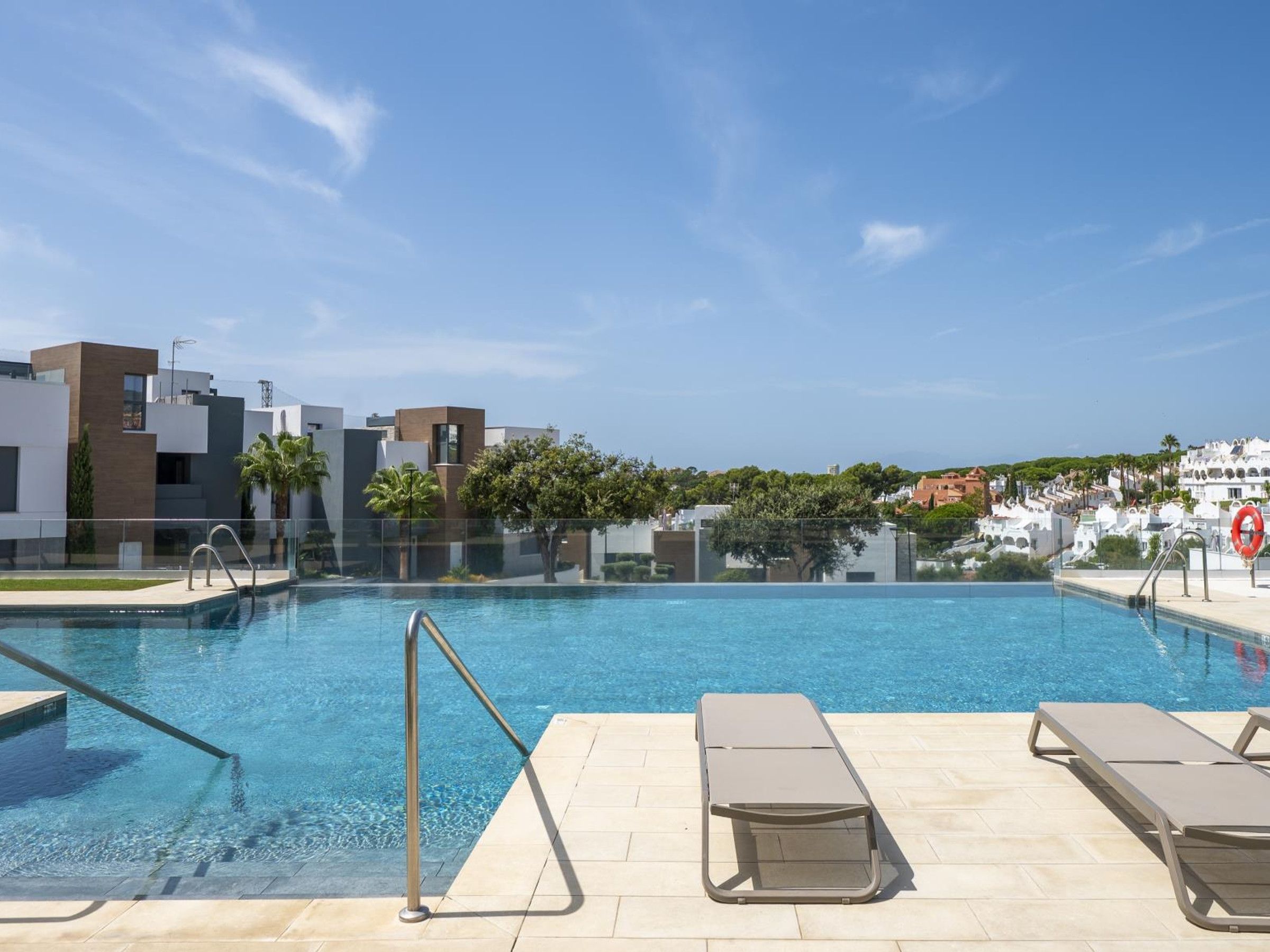 Una piscina con agua azul cristalina, rodeada de edificios modernos y un cielo despejado.