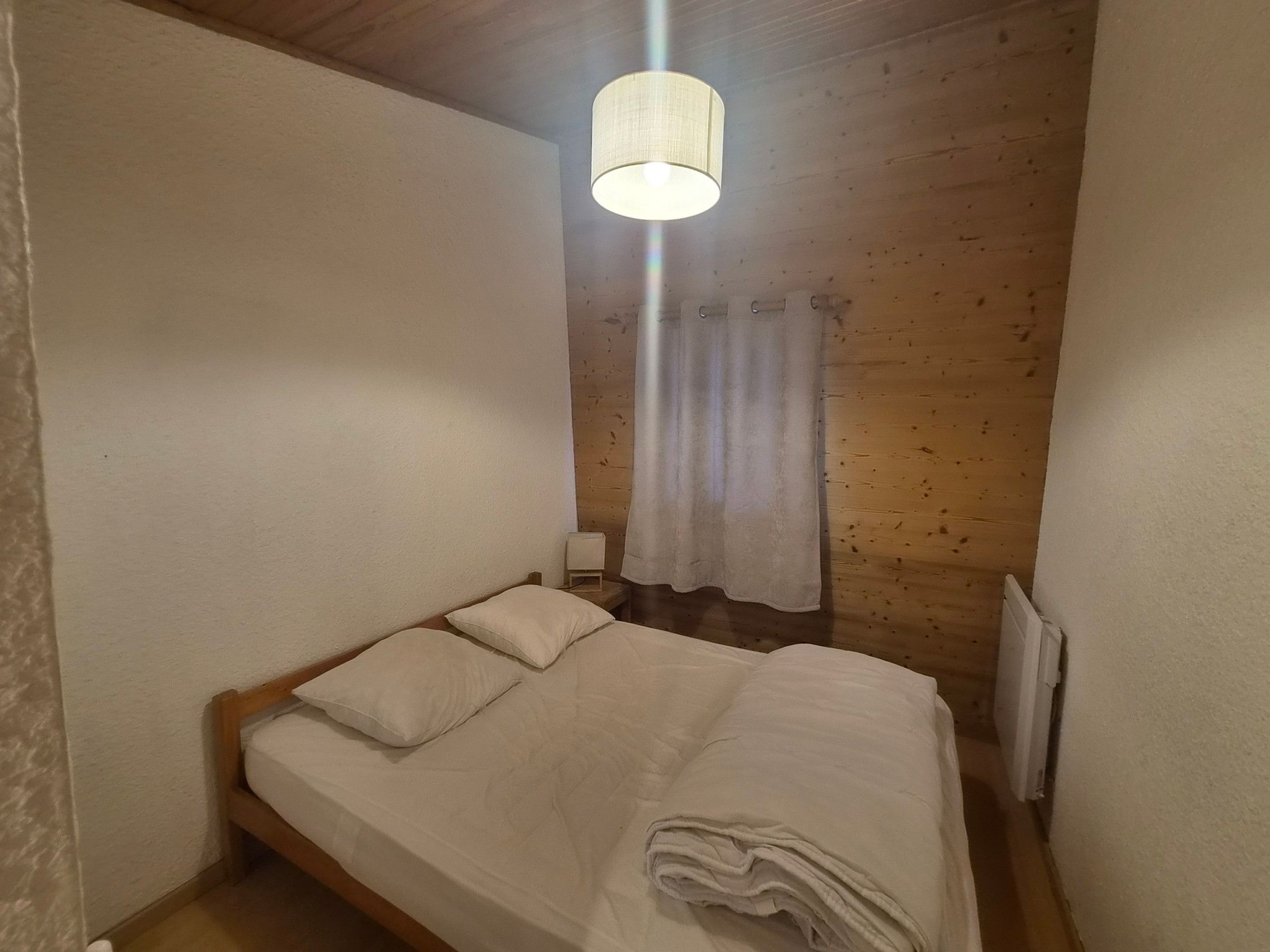 Une petite pièce agréable, dotée d’un lit simple, d’une table de chevet, d’une lampe et d’une fenêtre avec un rideau.