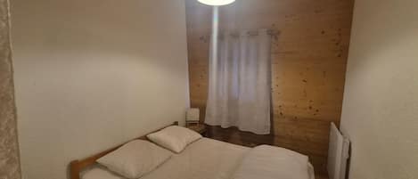 Une petite pièce agréable, dotée d’un lit simple, d’une table de chevet, d’une lampe et d’une fenêtre avec un rideau.