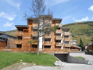 A multi-story wooden building with balconies, named "LES ALBERGES," set in a hilly area with a clear sky. - Ideal duplex in Les Deux Alpes - 6 guests (Les Deux Alpes)