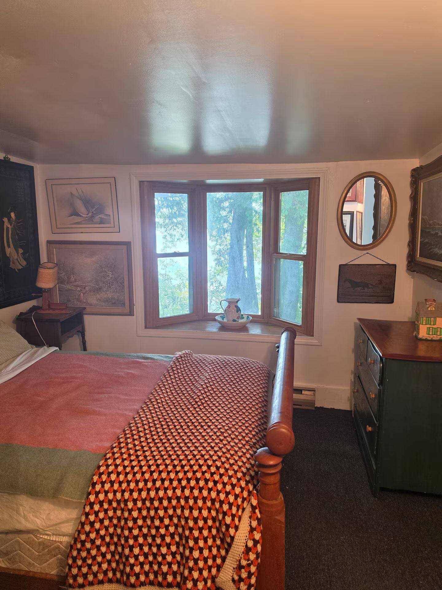 Une chambre à coucher avec un lit, une commode, une fenêtre donnant sur un beau paysage et un miroir.