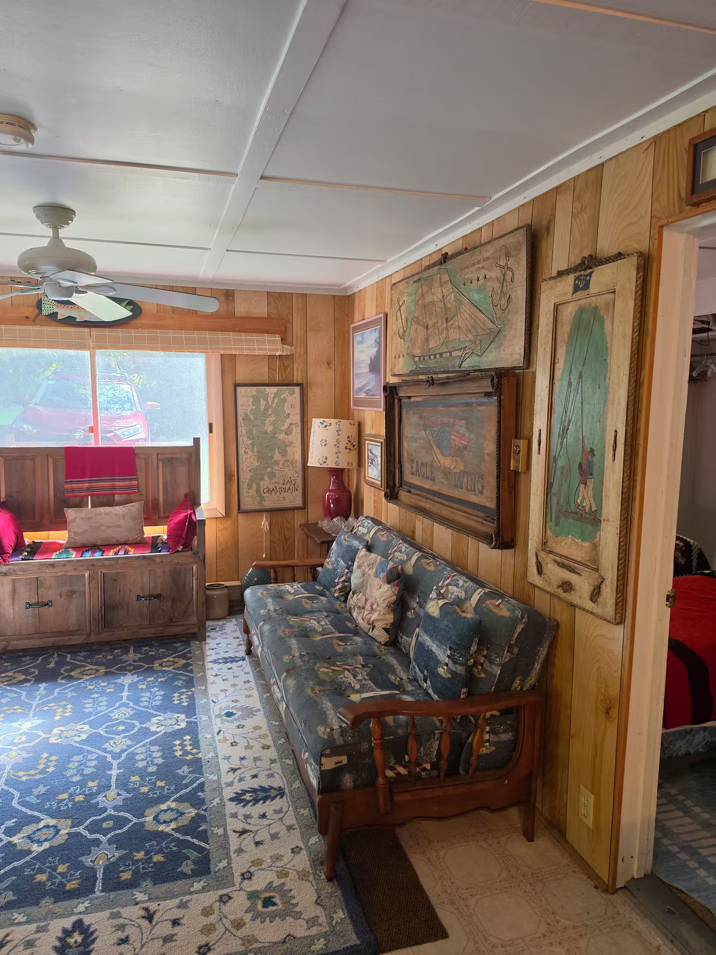 A cozy room with a wooden floor, a patterned rug, a sofa, a wooden cabinet, and a ceiling fan.