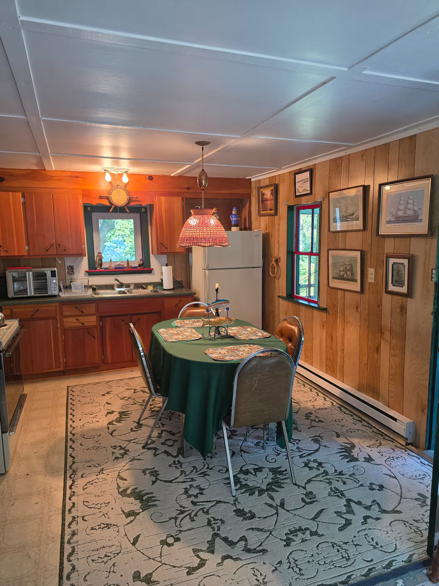 Una cocina acogedora con paredes de madera, una mesa de comedor con sillas, un televisor y un refrigerador.