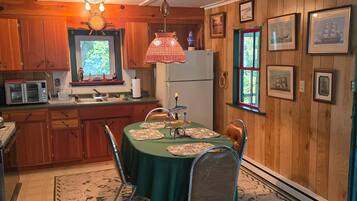 Una cocina acogedora con paredes de madera, una mesa de comedor con sillas, un televisor y un refrigerador.
