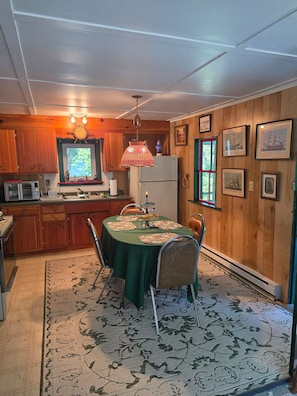 A cozy kitchen with wooden walls, a dining table with chairs, a television, and a refrigerator.