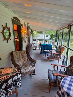 Un porche cubierto con muebles de mimbre, una mesa con mantel azul y adornos en las paredes.