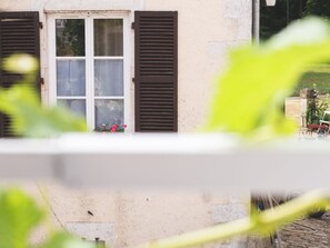 A building with a window and shutters, a visible door, and a garden area with a bench and a hose. - Charming quiet cottage - 2 guests (Choloy-Ménillot)