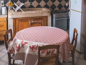 Een keuken met een eettafel bedekt met een tafelkleed met stippen, houten stoelen, een fornuis en een koelkast.