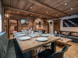 A wooden interior with a long dining table set for a meal, a sofa, and a mounted animal skull. - Cozy apartment in village center - 8 guests (La Clusaz)