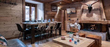 Ein rustikales Interieur mit Holzbalkendecke, Kamin, Essbereich mit Stühlen und einer Couch.